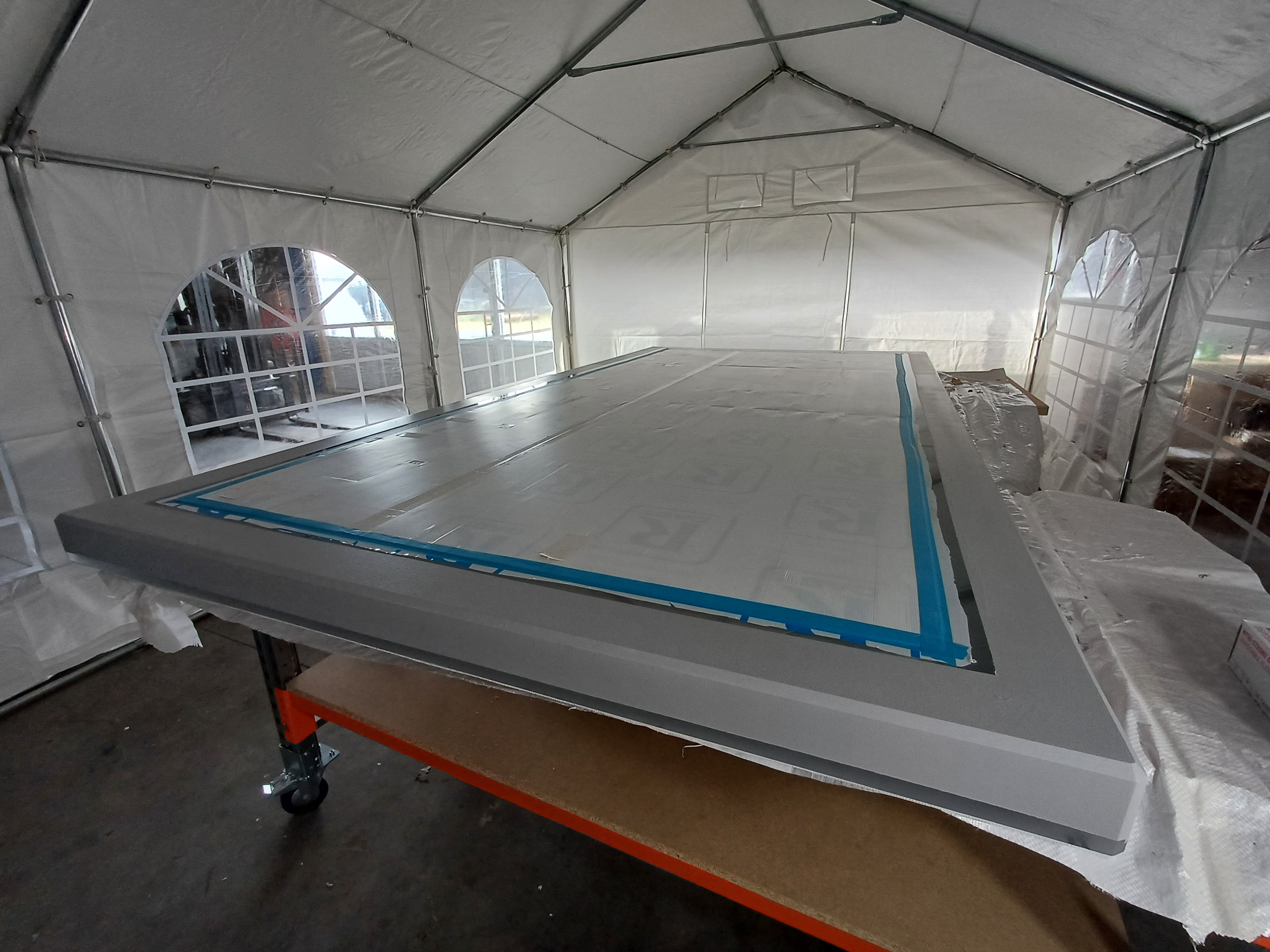 A large, rectangular acrylic pannel covered with protective material, set up inside a tent with white fabric walls and circular windows.